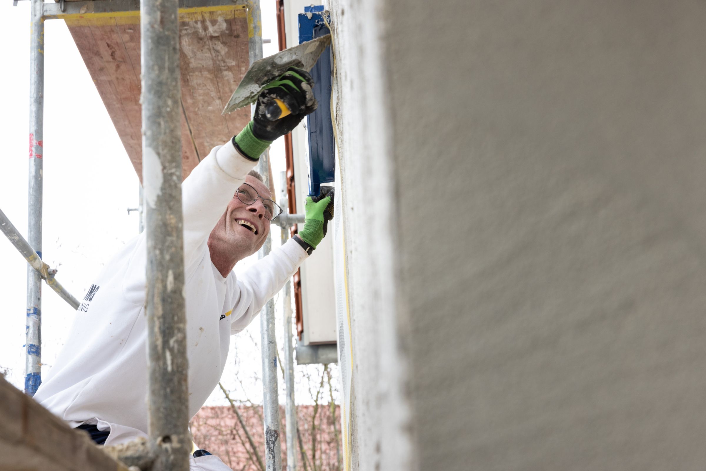 Handwerker arbeitet lächelnd an einer Fassade auf einem Baugerüst