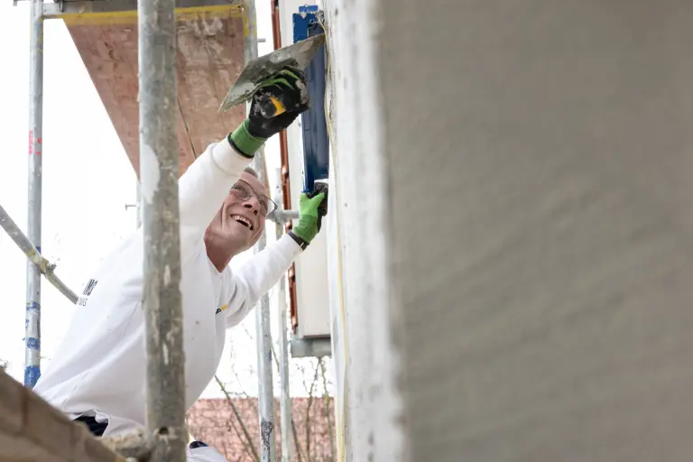 Handwerker arbeitet lächelnd an einer Fassade auf einem Baugerüst