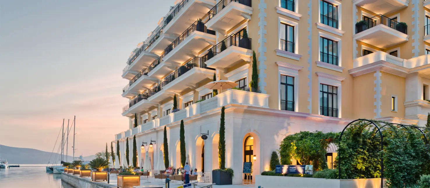 Elegantes Uferhotel mit gelber Fassade, vielen Balkonen und Abendbeleuchtung.