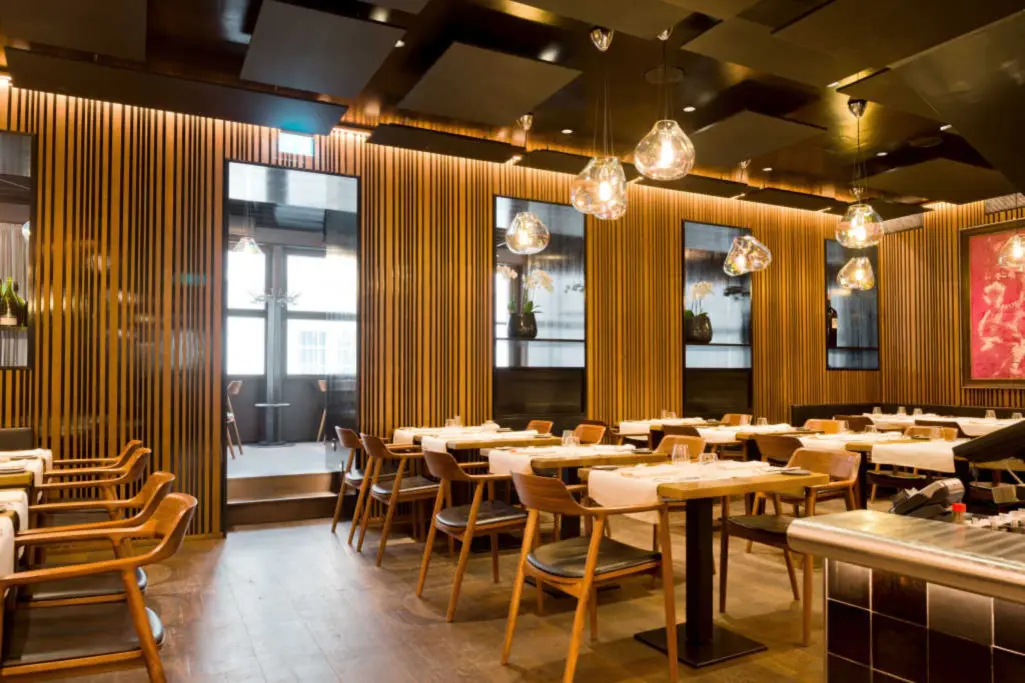 Designrestaurant mit Holzlamellenwänden, schwarzen Akustikdecken und warmen Glaskugel-Pendelleuchten