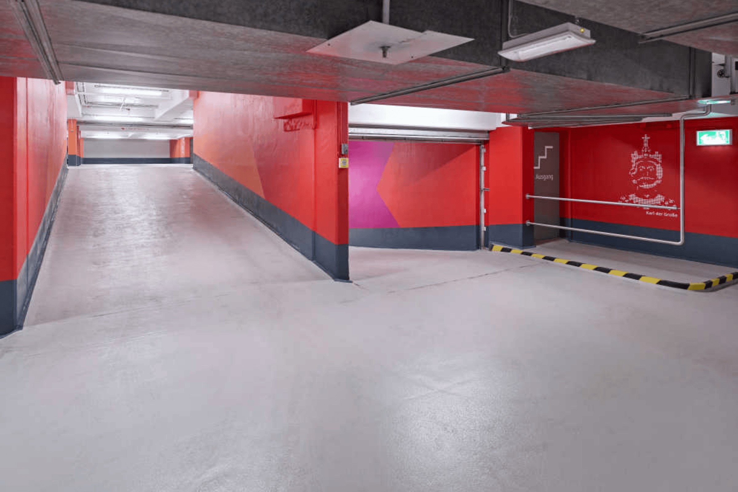 Rote Parkhausrampe mit hellgrauem, rutschhemmendem Boden und gelb-schwarzer Barriere.
