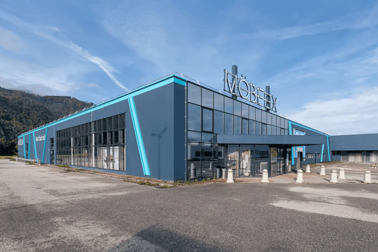 Möbelix in Wels mit großflächiger Glasfassade und auffälligen türkisblauen Akzentstreifen
