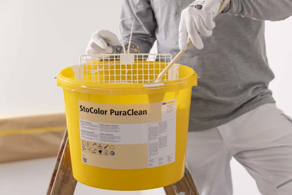 Gelber StoColor-PuraClean-Farbeimer, Arbeiter rührt die Farbe an.