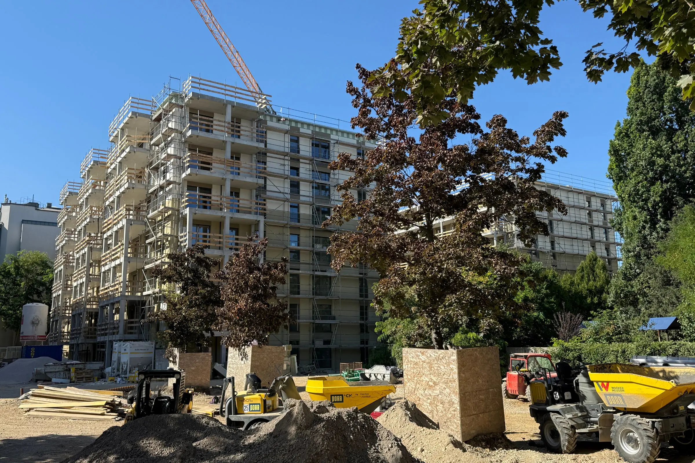 Baustelle im Leopoldquartier Wien mit eingerüstetem Wohngebäude, Baumaschinen und geschützten Bäumen