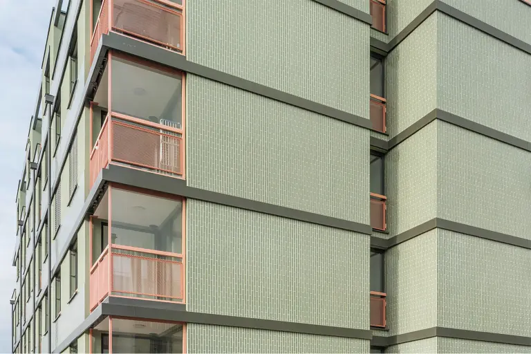 Innenhof des Wohnprojekts „Orchidea“ im Kennedy Garden, Wien: U-förmiger Bau mit hellgrünen, keramisch strukturierten Fassaden, lachsfarbenen Balkonen und gemeinschaftlichem Hof mit Spielbereich.